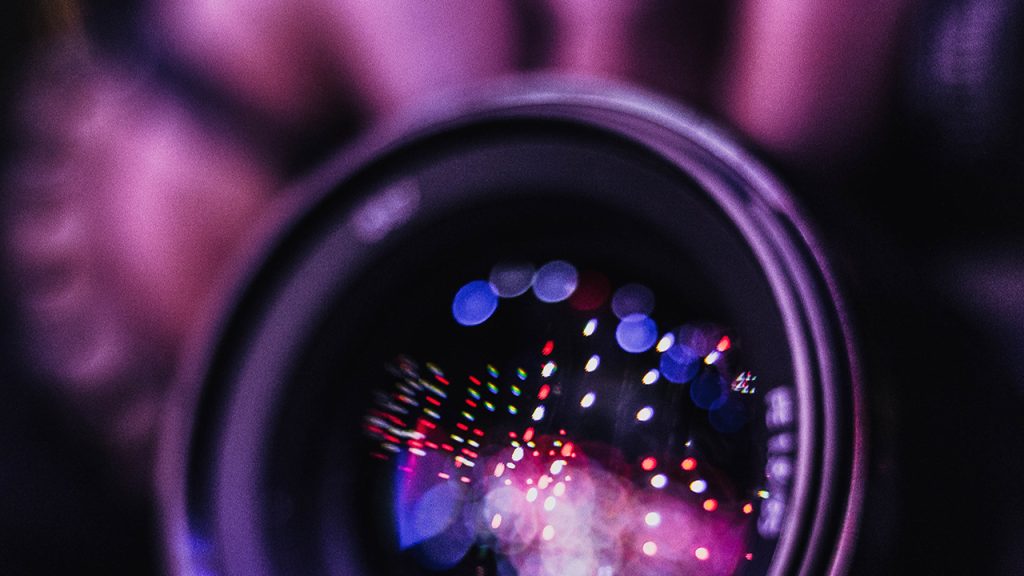 a close up image of a camera lens with purple colours in the background and reflected on the glass lens