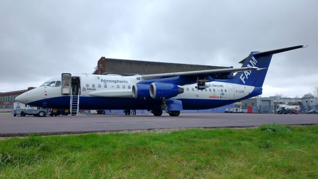 Large white and blue research aircraft stationary on a runway with a set of stairs leading into the aircraft