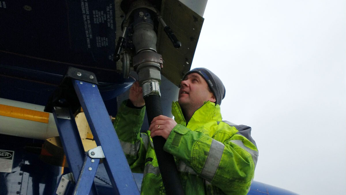 Person wearing high-visibility jacket holds a large hose to refuel an aircraft
