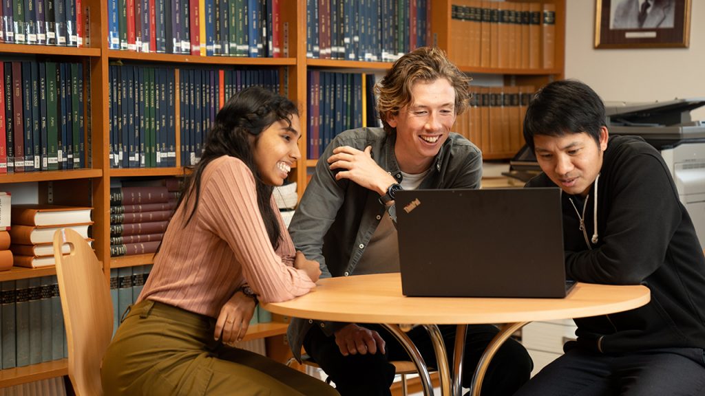 A group of three people sat at a round table, looking at a laptop.