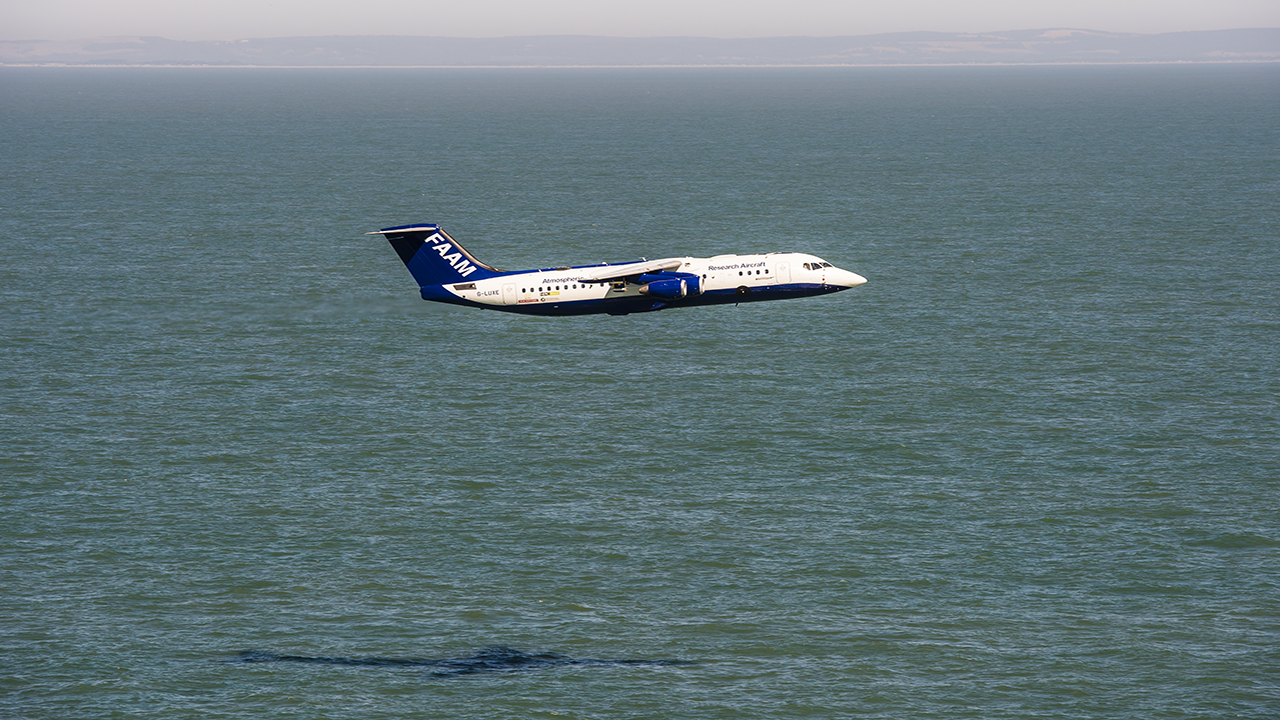 Blue and white research aircraft flying low over blue water.