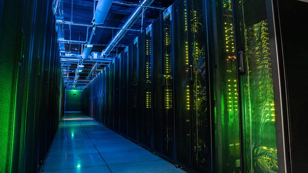 Dark aisle full of racks of computer servers illuminated by small green and blue equipment lights.