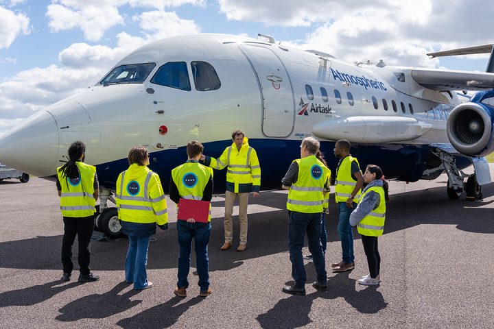 7 people wearing hi vis jackets in front of a white and blue aircraft