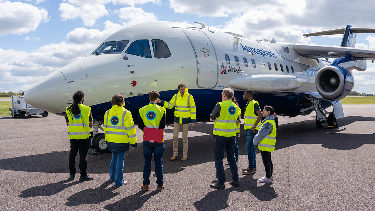 7 people wearing hi vis jackets in front of a white and blue aircraft
