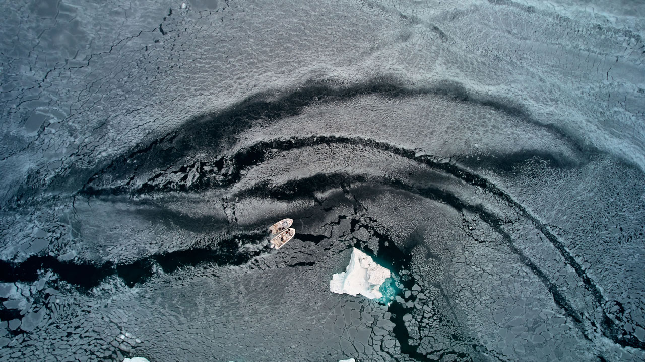Aerial view of two small boats breaking a path through melted sea ice.