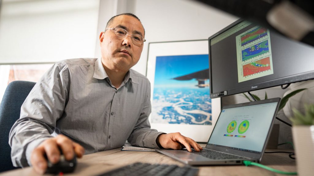 Man sits looking at two computer screens with scientific models on.