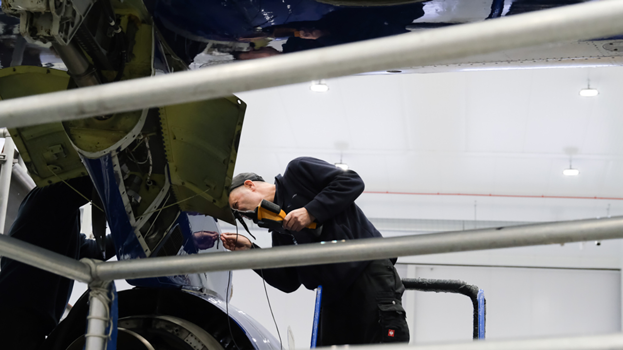 A person holding a piece of engineering equipment inspecting an engine mount on a large blue and white research aircraft.