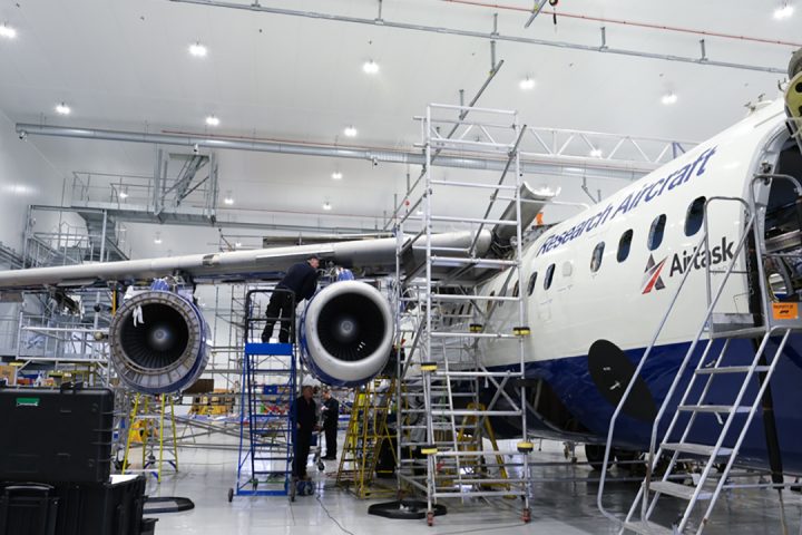 A large blue and white research aircraft in a hangar. It has scaffolding around it and is undergoing maintenance.