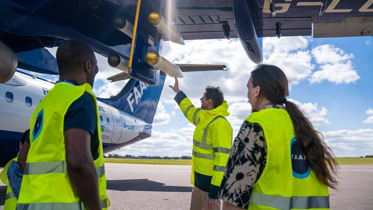 Three people stand looking at the FAAM aircraft in high-vis jackets.