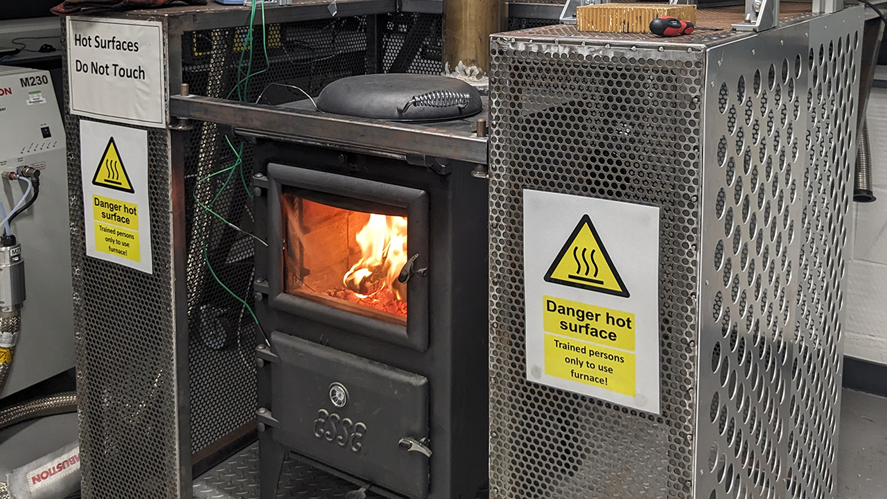 A lit wood burner stove inside a protective metal unit, inside a research laboratory