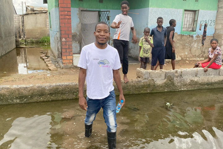A person wearing wellies stands in floodwater in a residential area in Africa