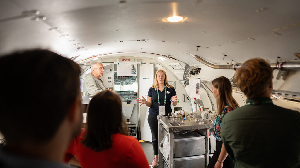 A group of people on a tour, stood on the inside of an aircraft fitted out with scientific instruments.