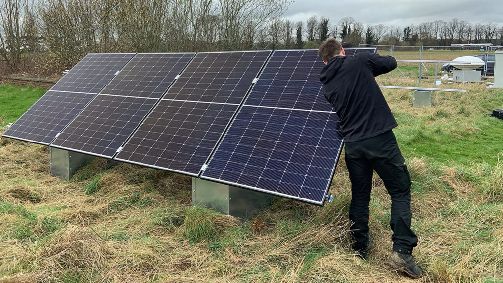 Person wearing dark coloured clothing fixes a solar panel