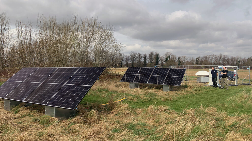 Solar panels in a field and two people stood nearby looking at them.