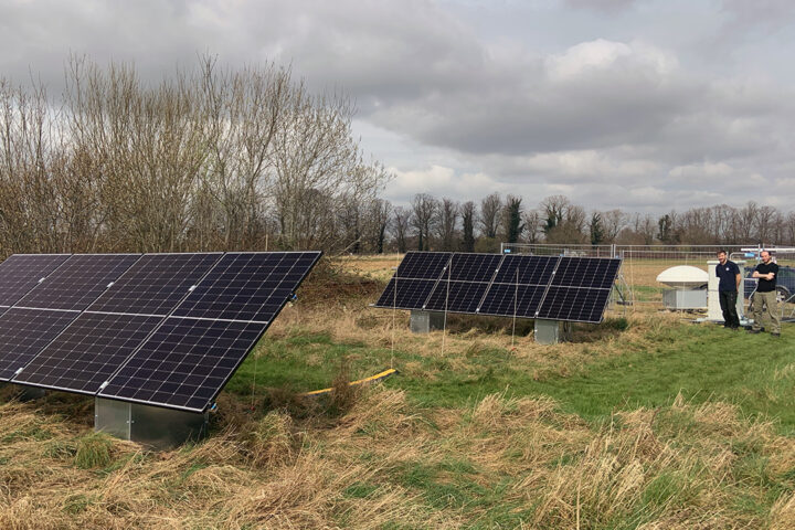 Solar panels in a field and two people stood nearby looking at them.