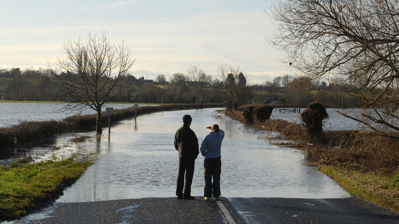 Two people looking at a road flooded by a river.