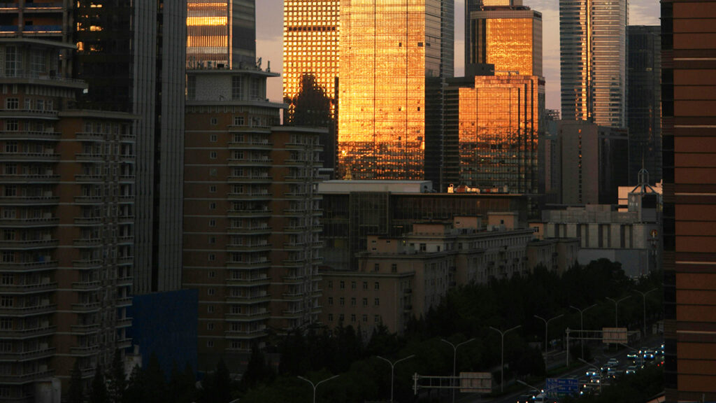 Warm sunlight reflected off tall building in a city, with the head lights of cars in traffic seen below