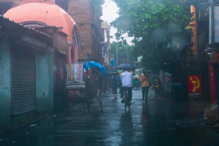 People carrying umbrellas walking and cycling on a rainy street in India.