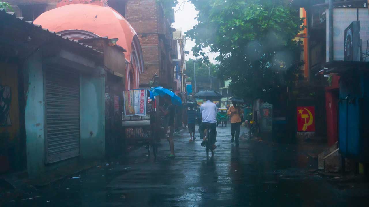 People carrying umbrellas walking and cycling on a rainy street in India.