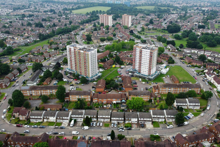 Aerial view of tower blocks and other housing in a suburb with cars parked and driving on the streets.