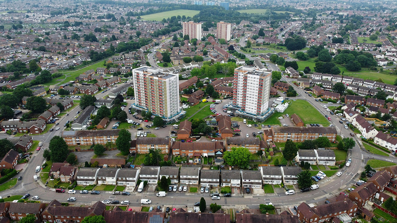 Aerial view of tower blocks and other housing in a suburb with cars parked and driving on the streets.