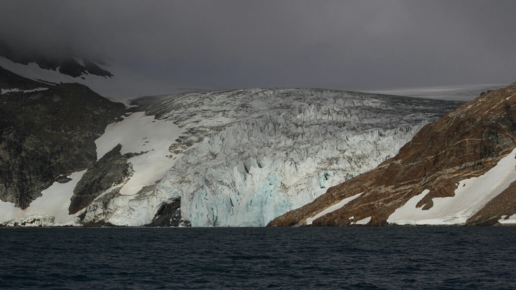 Glacier melting into ocean, surrounded by rocky outcrops.