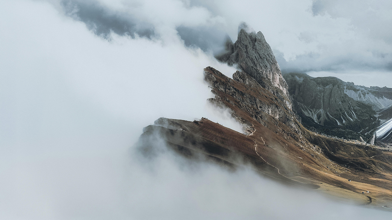 White clouds push up against the crest of a mountain