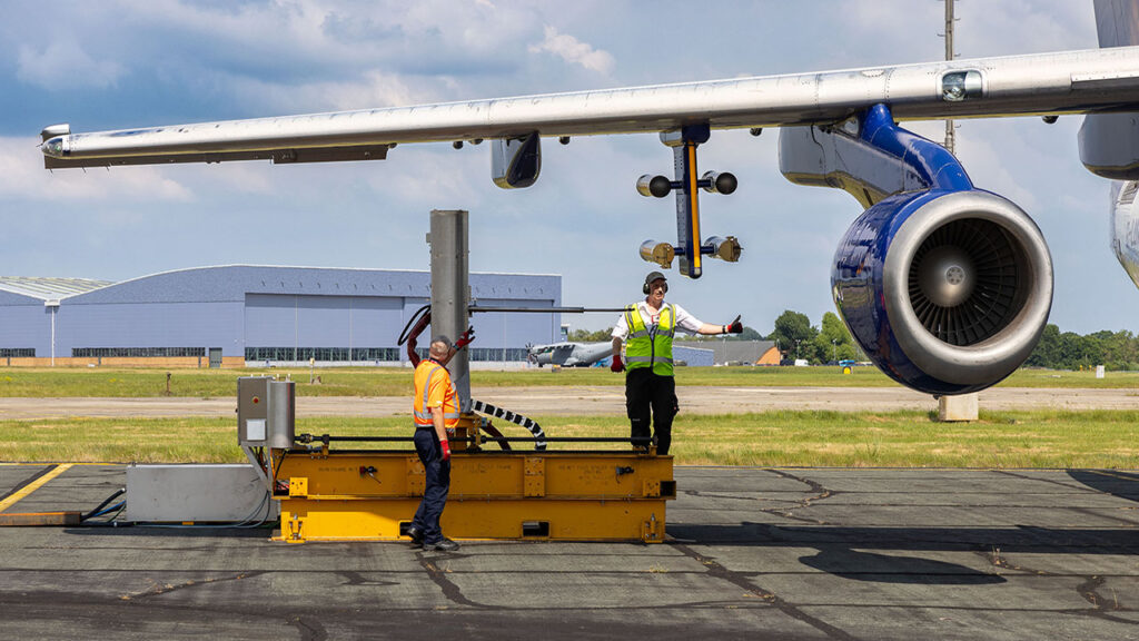 2 people stand underneath the wing of an aircraft setting up a scientific instrument.