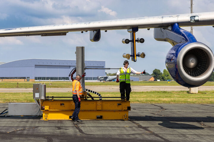 2 people stand underneath the wing of an aircraft setting up a scientific instrument.