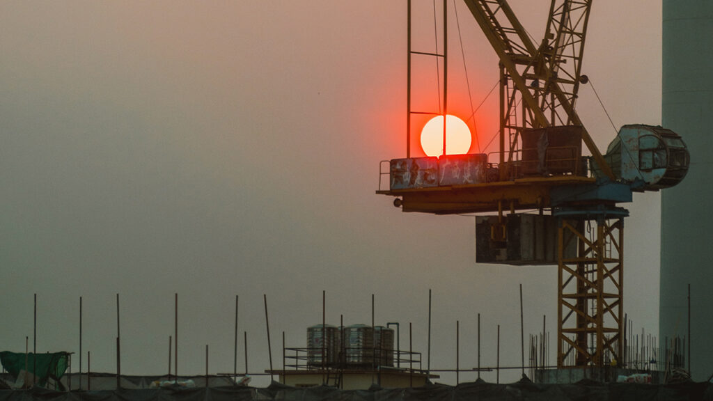 Hazy sky with setting sun, behind the silhouette of cranes and a building site