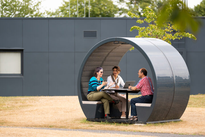 Three people sat at a table, with a laptop, inside a circular outdoor meeting pod