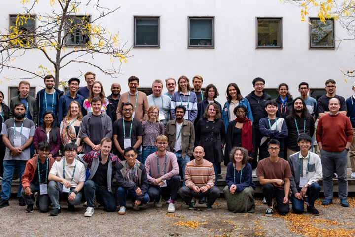 Large group of people stood or sat in front of a white building, facing the camera and posing for a picture.