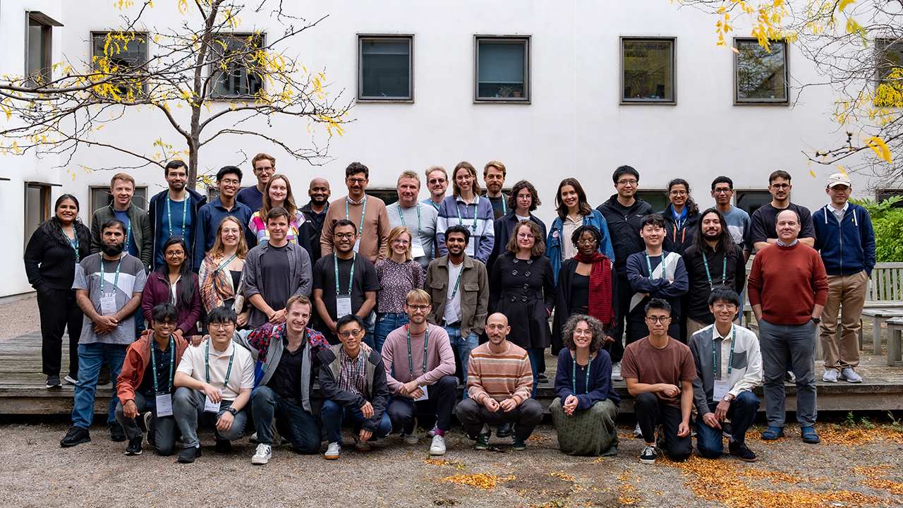 Large group of people stood or sat in front of a white building, facing the camera and posing for a picture.