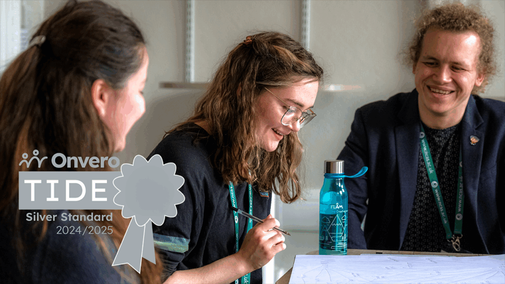 three people sat looking at a piece of paper on a table, and there is a silver-grey award logo over the top of the image