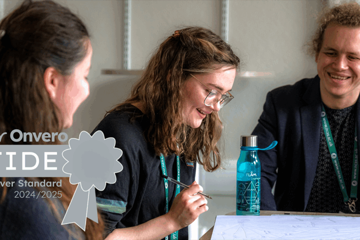 three people sat looking at a piece of paper on a table, and there is a silver-grey award logo over the top of the image