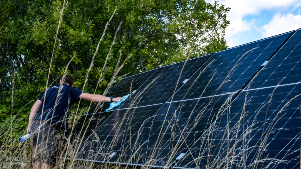 Person using a cloth to clean solar panels in a field