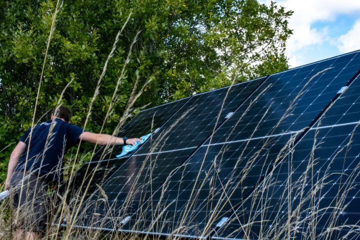 Person using a cloth to clean solar panels in a field