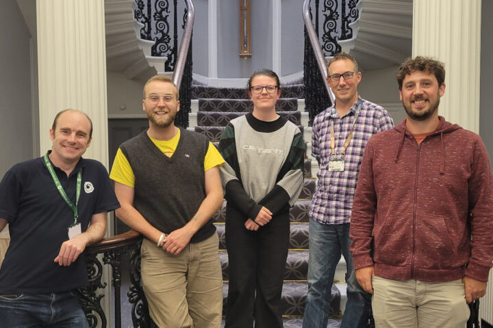 5 people stand in a line in front of a grand staircase