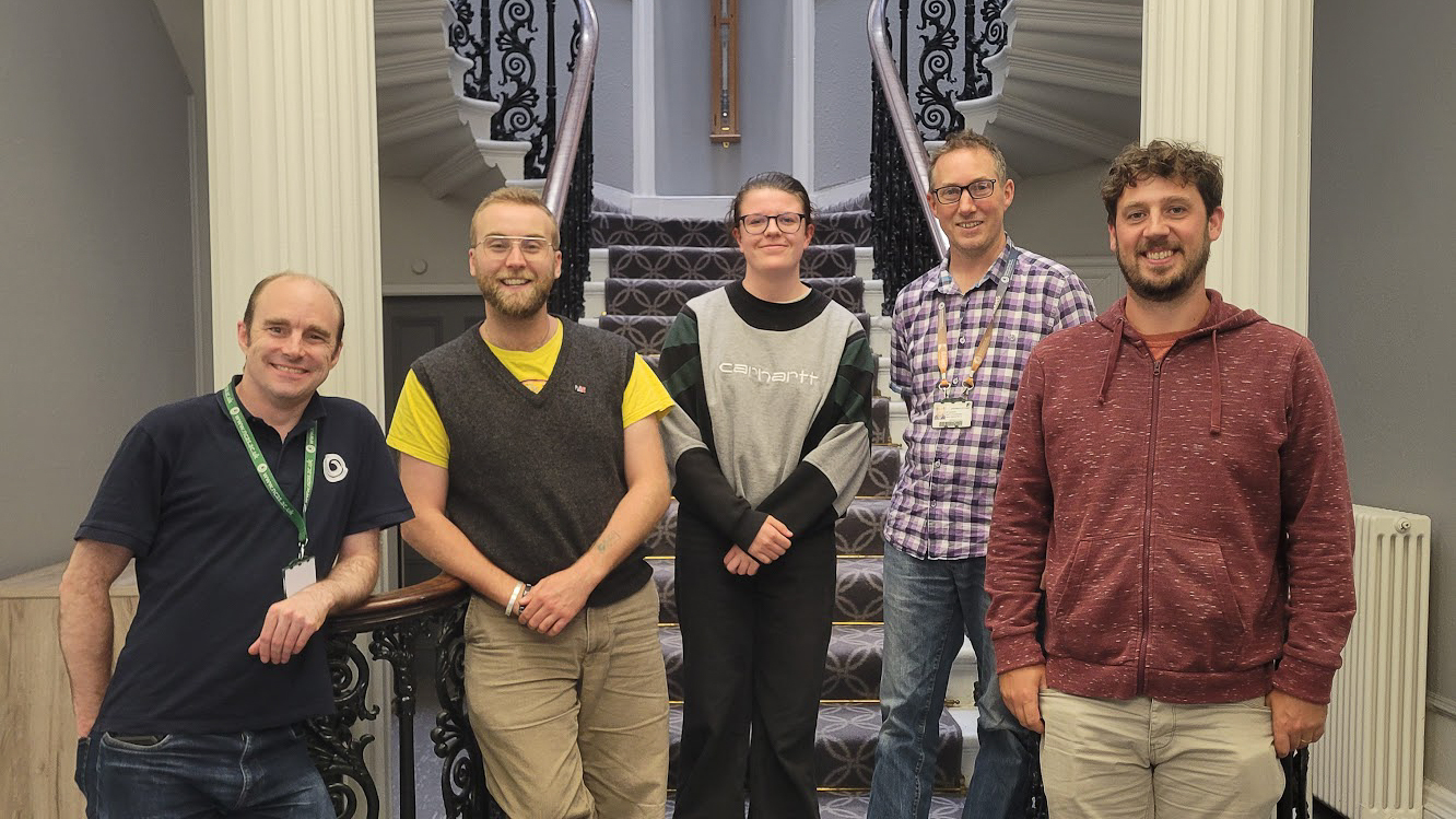 5 people stand in a line in front of a grand staircase