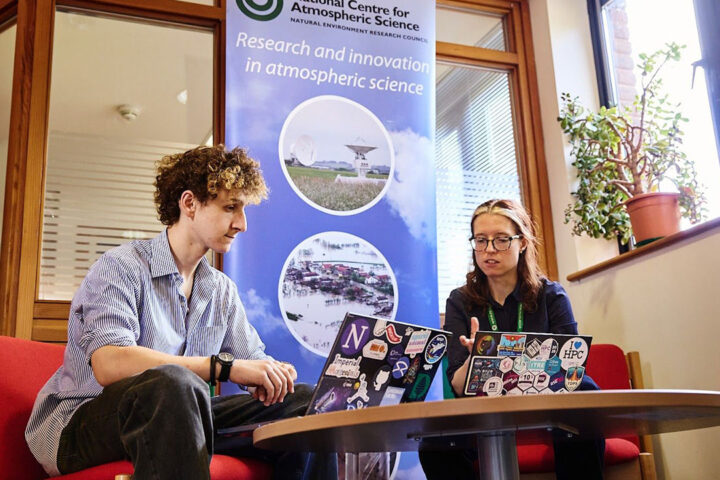 Two people sat on red chairs at a small round low table, looking at their laptops.