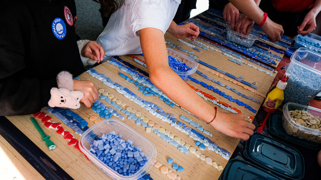 Young people place small blue and red mosaic tiles in lines onto a wooden board.