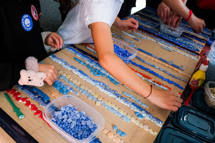 Young people place small blue and red mosaic tiles in lines onto a wooden board.