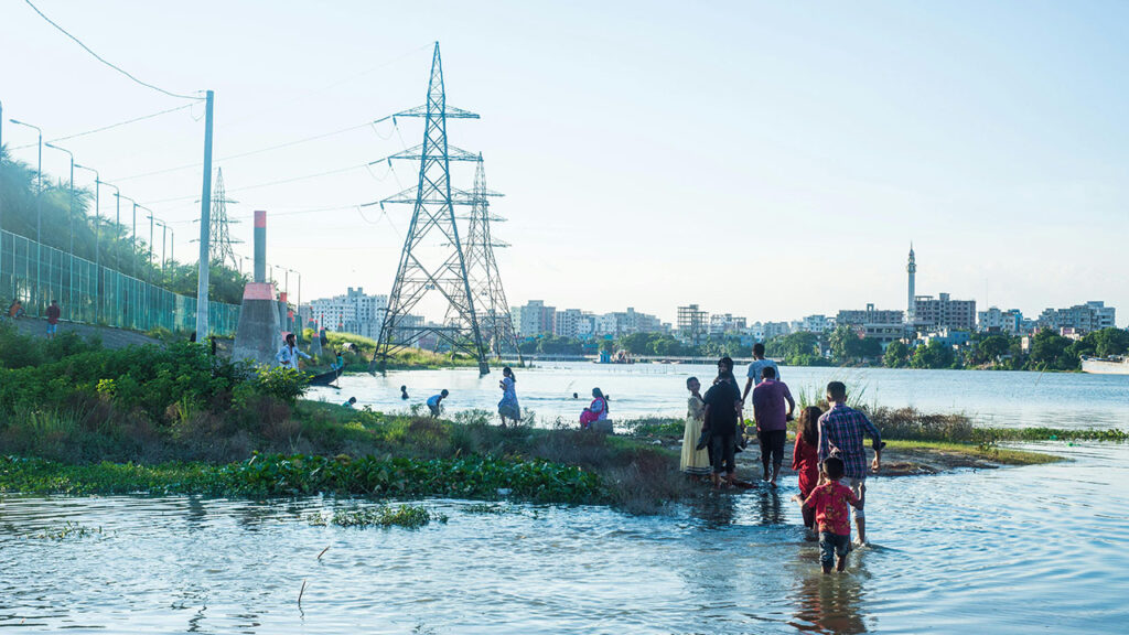 A group of people walk through flooded ground, with electricity power lines in the distance.