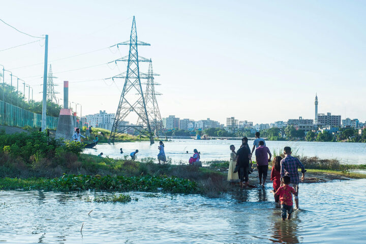 A group of people walk through flooded ground, with electricity power lines in the distance.
