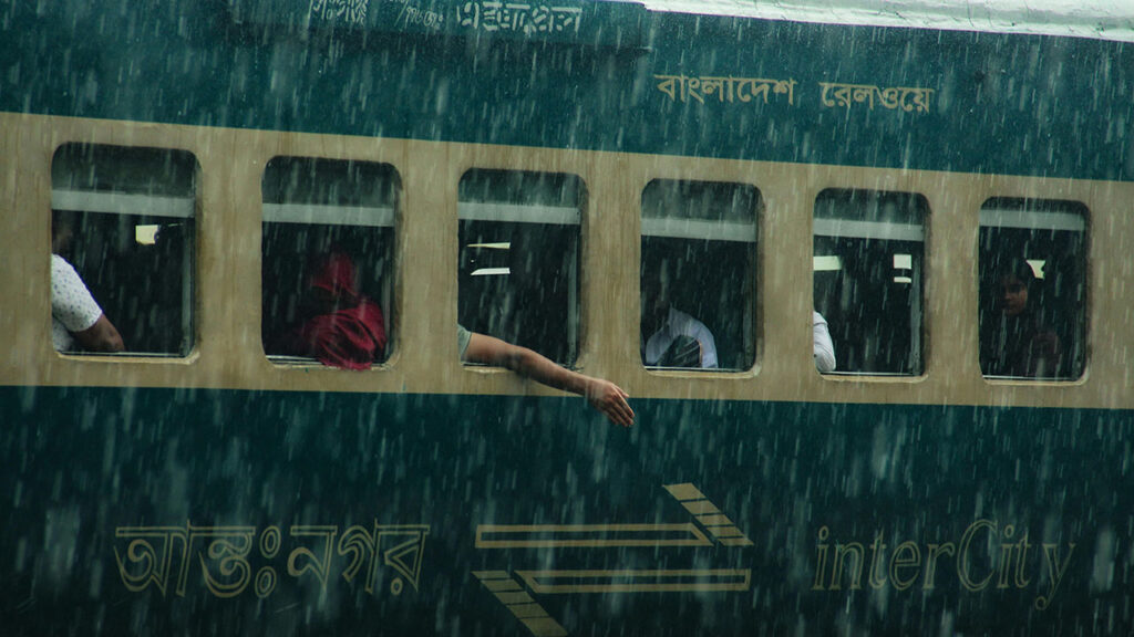 A person reaching their arm out of a train window into heavy rain.