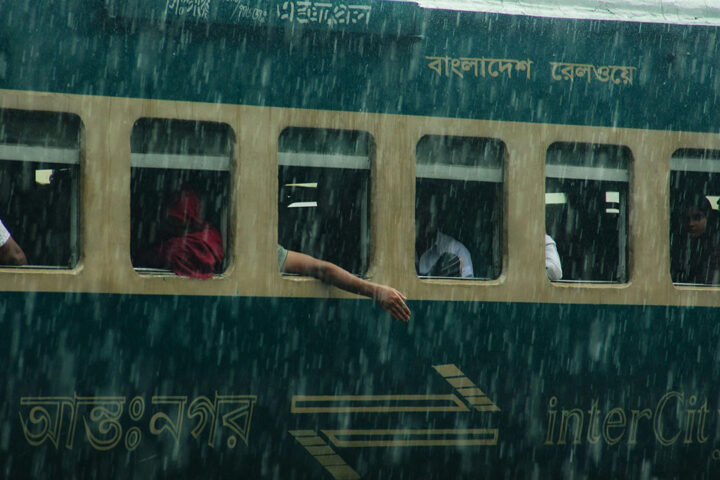 A person reaching their arm out of a train window into heavy rain.
