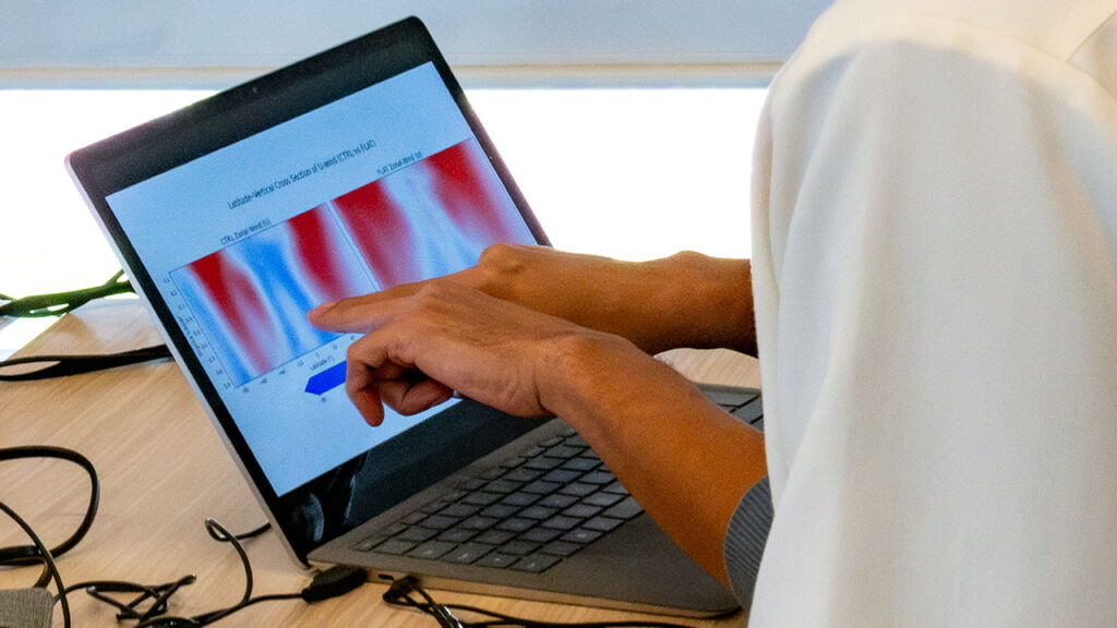 A person's hands pointing at a laptop screen. On the laptop screen there is a white, red, and blue graph on display.