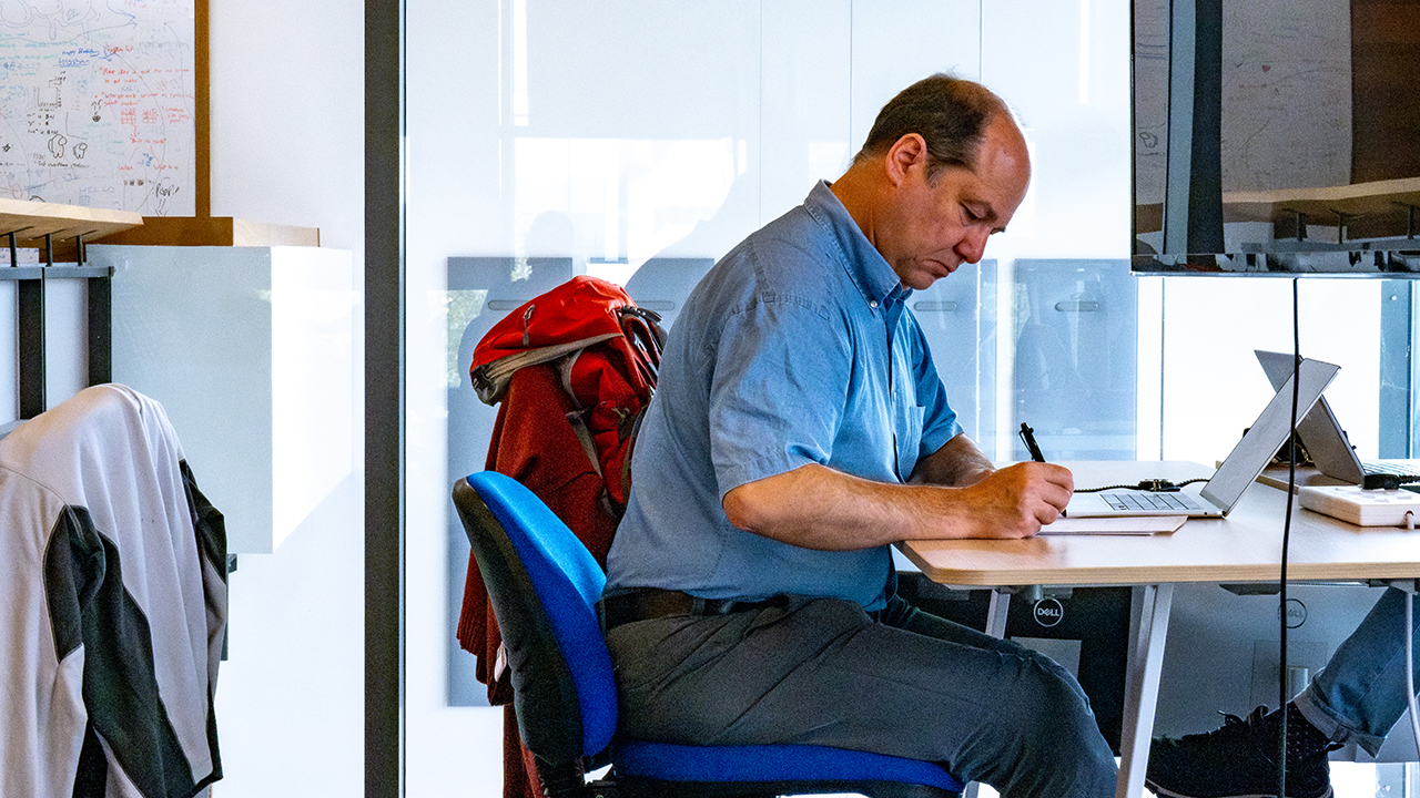 Person wearing blue shirt sits writing at a desk.