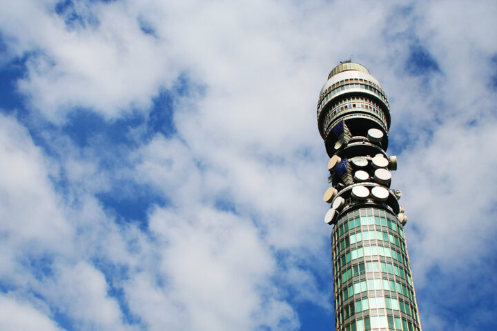 Blue sky with white fluffy clouds, and a round tall tower with satellite dishes on it.