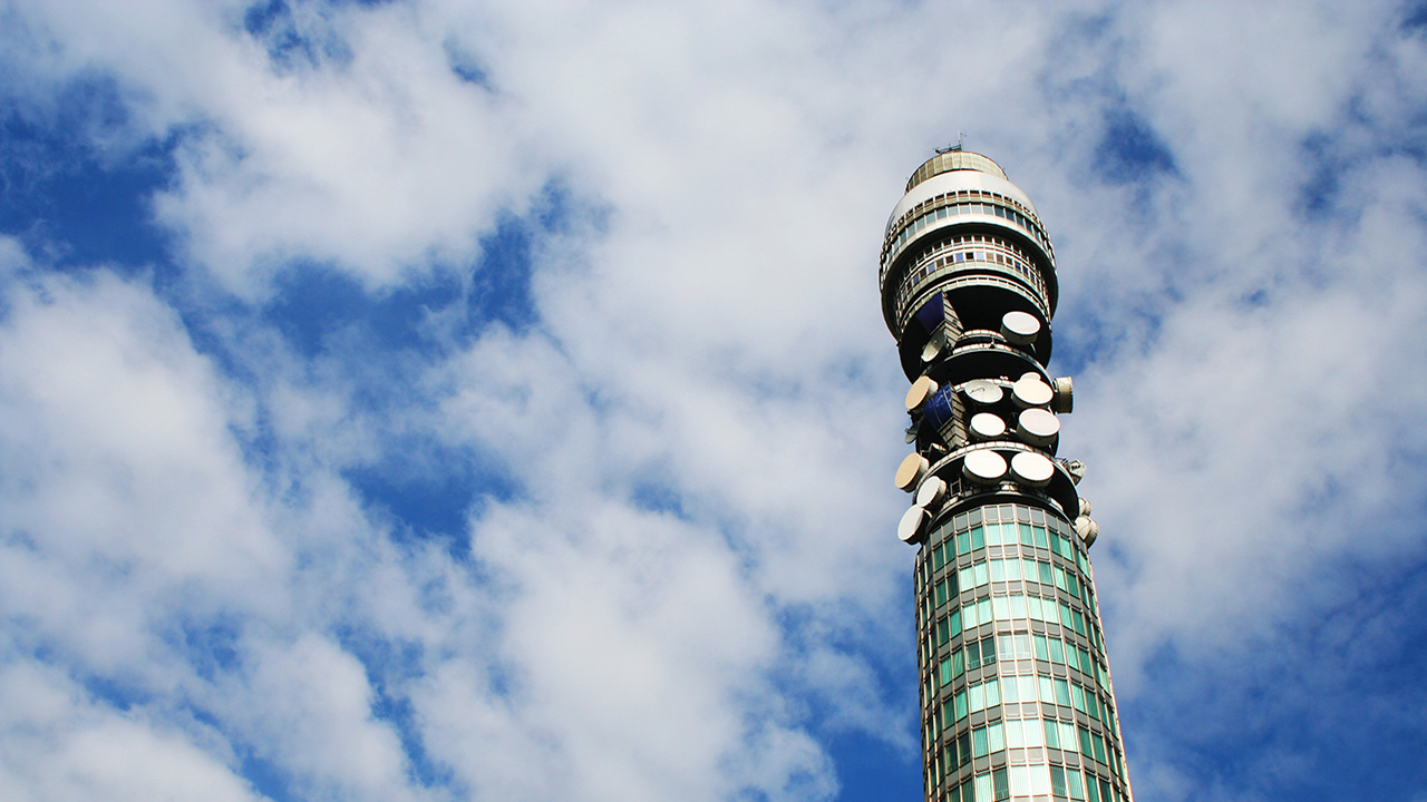 Blue sky with white fluffy clouds, and a round tall tower with satellite dishes on it.